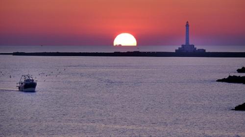 a boat in the water at sunset with a lighthouse at AMA Apartment Stella in Gallipoli