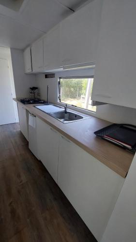 une cuisine avec des armoires blanches, un évier et une fenêtre dans l'établissement Logement dans propriété, à Saint-Laurent-dʼAigouze