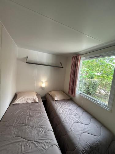 two beds in a small room with a window at mobil home AU SOLEIL in La Roque-dʼAnthéron