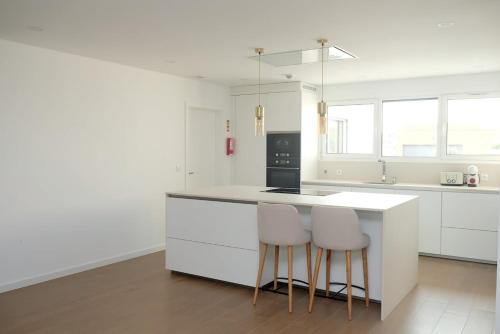 una cucina con armadi bianchi e un bancone con due sgabelli di Olive House - 4 bedrooms a Gafanha da Nazaré