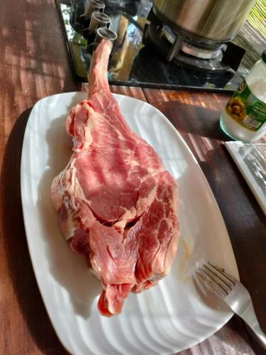 a piece of meat on a white plate with a fork at La maison in Gandoca