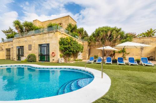 a swimming pool in front of a house with chairs and umbrellas at Zest Holiday Home in Qala