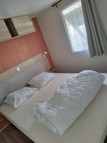 Cette chambre comprend un lit avec des draps blancs et une fenêtre. dans l'établissement Mobil-home 