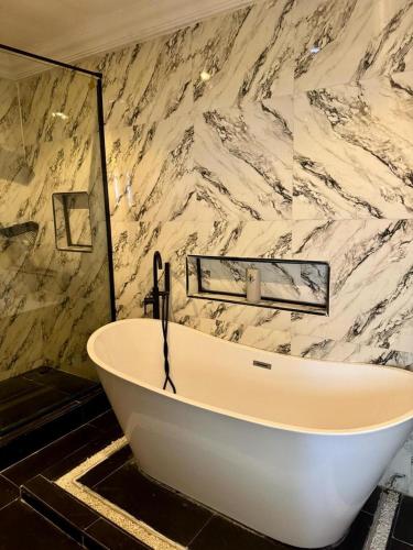 a white bath tub in a bathroom with a marble wall at Shortlet By Loveline in Ibadan