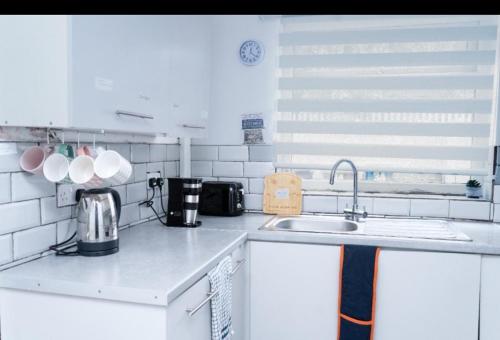 a kitchen with white counters and a sink and a window at Spacious and Comfy Pad - Perfect for Long Stays & Contractors - Close to Sports Village, Leigh Market, and Mesnes Park - Easy Parking - Speedy Wi-Fi - Free On-Site or Nearby Parking - Private Luxury Garden in Leigh