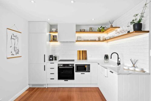 a white kitchen with a sink and a stove at Wombarra Luxe Cottage in Wombarra