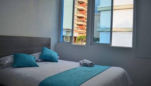 a bedroom with a bed with blue pillows and two windows at Hotel Éxito Pereira Center in Pereira