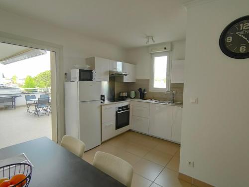 une cuisine avec des appareils électroménagers blancs, une table et une horloge dans l'établissement Appartement T2 proche plage avec terrasse, clim, Wi-Fi et parking - FR-1-781-102, à Valras-Plage