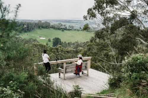 Un par de personas de pie en un banco de madera en The Ridge House - Stylish Gippsland Getaway, en Yarragon