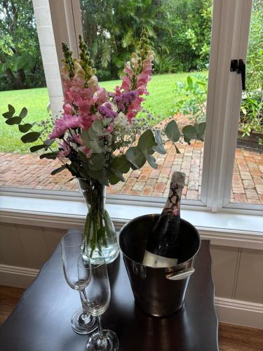Una botella de champán y un jarrón de flores sobre una mesa. en Mitta Glen Guesthouse, en Flaxton