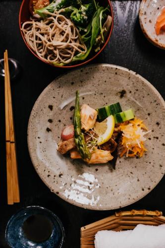 a plate of food with vegetables and noodles on a table at Shizuka Ryokan Japanese Country Spa & Wellness Retreat in Hepburn Springs