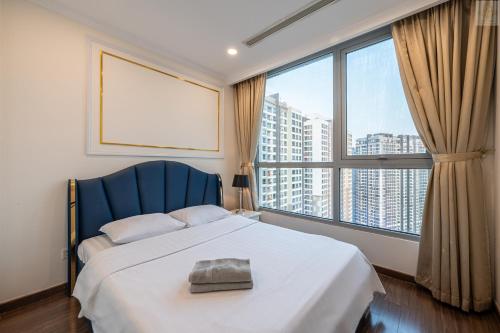 a bedroom with a bed with a blue headboard and large windows at Landmark Plus Vinhomes CityView Suite in Ho Chi Minh City