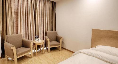 a bedroom with two chairs and a bed and a table at GreenTree Alliance Suzhou Zhangjiagang Nanfeng Town Hotel in Zhangjiagang