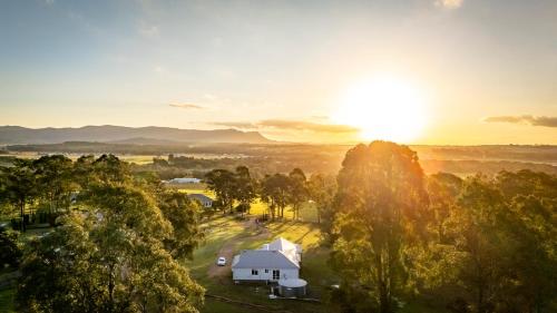 a house in the middle of a field with the sunset in the background at Coopers Lodge, Lovedale - A rural escape in the heart of wine country in Lovedale