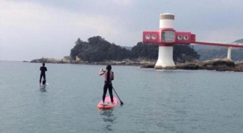 two people on a paddle board in the water with a lighthouse at AKISAWA HOTEL in Shimanto