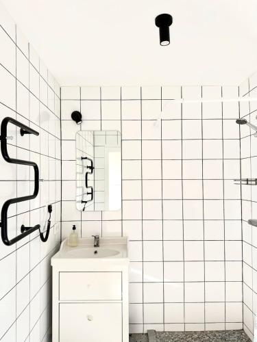 a white tiled bathroom with a sink and a shower at Svencele mini cottage apartment in Svencelė