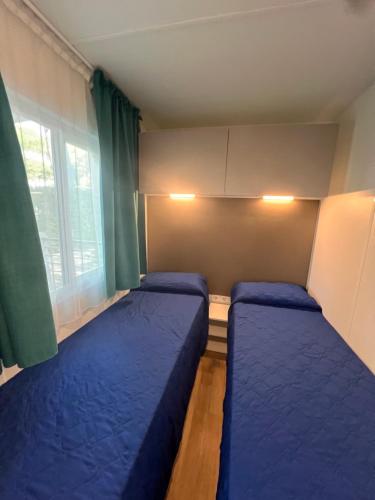 a small room with two blue beds and a window at Dune Prestige & Chalets in Bibione