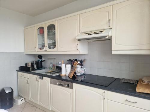 une cuisine avec des armoires blanches et un comptoir noir dans l'établissement T4/5 avec vue sur les Alpes à 5 minutes de Lyon, à La Mulatière