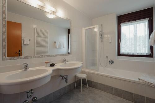 a white bathroom with two sinks and a shower at Hotel Alpenrose in Carezza al Lago