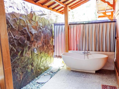 a bathroom with a tub and a large stone wall at Anggi Villas Ubud in Tegalalang
