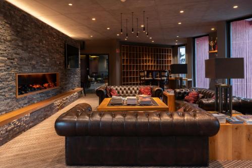 a living room with a leather couch and a fireplace at L'Hôtel et Restaurant du Golf de Clervaux in Eselborn