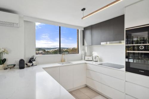 a kitchen with white cabinets and a large window at Inner City Harbour Views With Parking in Sydney