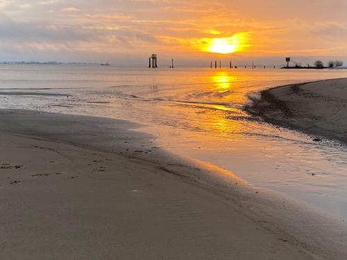 a sunset on a beach with the sun setting at Ferienwohnung Rehkitz in Drochtersen