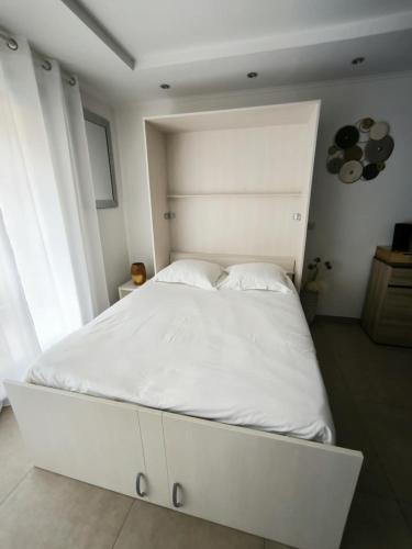 un lit blanc dans une chambre blanche avec une grande fenêtre dans l'établissement Studio à 2 minutes de la plage, à La Grande Motte