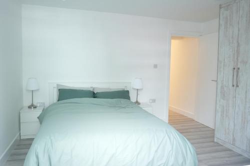 a white bedroom with a large white bed with blue pillows at Cosy Getaway near beach in Southend-on-Sea