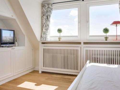 a bedroom with a bed and a tv and two windows at Ostertresker 78, DHH in Tinnum