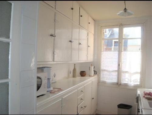 une cuisine avec des armoires blanches et un micro-ondes dans l'établissement le Tourbillon, à Mers-les-Bains