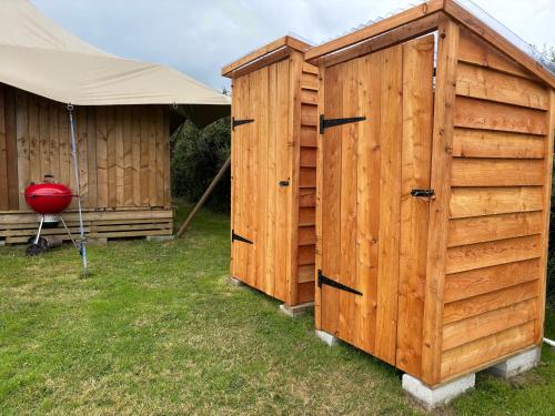 two wooden huts in the grass next to a tent at Tregantle Farm Eco GLAMPSITE in Torpoint