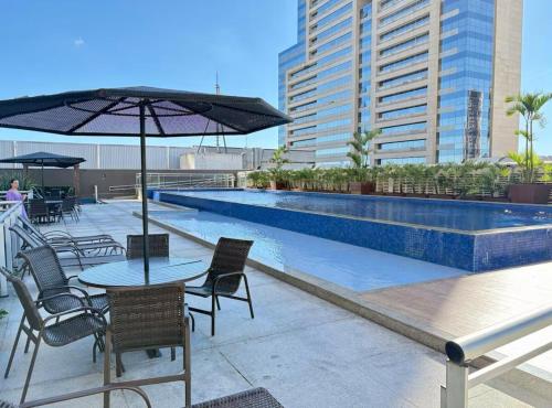 une table et des chaises avec un parasol à côté d'une piscine dans l'établissement Apto aconchegante no DF Plaza, à Brasilia