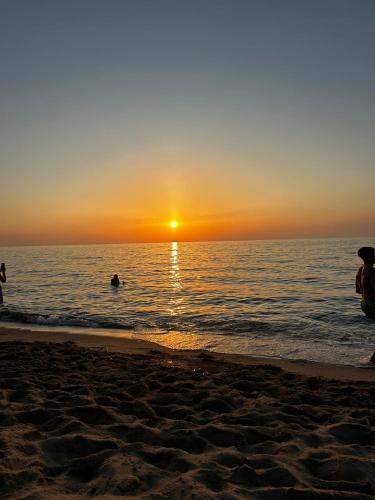 una puesta de sol en la playa con gente en el agua en Oro Verde, en Sedini