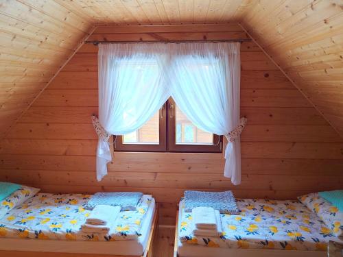 two beds in a log cabin with a window at Domki u Asi in Wilkasy