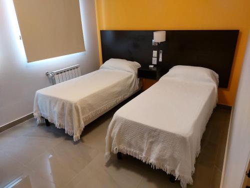 two beds in a hotel room with white sheets at Departamentos Rada in Rada Tilly