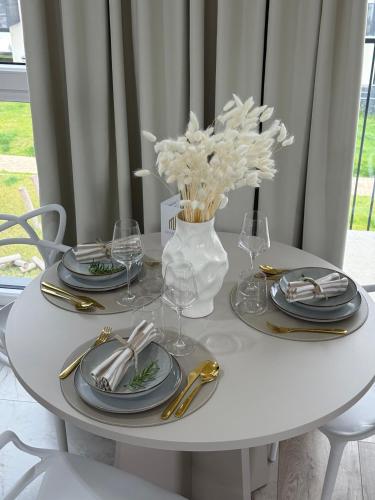 a white table with plates and glasses and a vase with flowers at GOLD Apartment - Lotnisko Katowice-Pyrzowice in Siewierz