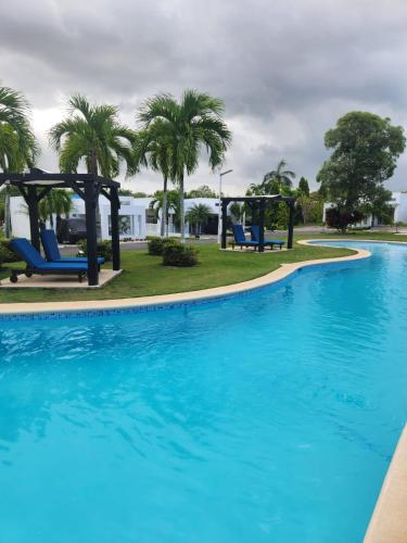 a large swimming pool with blue chairs and palm trees at Villa en Ibiza Residence II, disfruta en familia in Río Hato