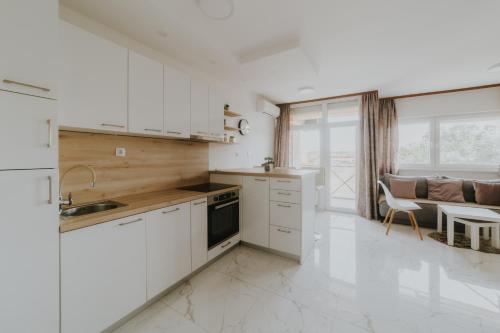 a kitchen with white cabinets and a living room at Apartmani MODUS - SELF-CHECK-IN in Virovitica