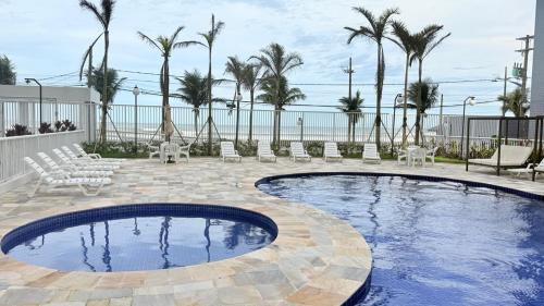 a swimming pool with chairs and palm trees at Refúgio do Aconchego Frente Praia Ocean Club in Mongaguá