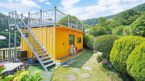 a small yellow house with a ladder in a yard at Geoje Sinbi Bada Pension in Geoje 
