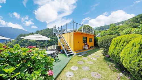 a small yellow house with a staircase in a yard at Geoje Sinbi Bada Pension in Geoje 