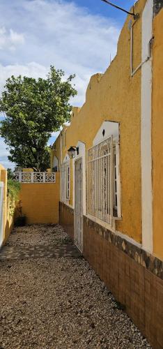 a yellow building with white gates and a tree at hotelito itzae in Izamal
