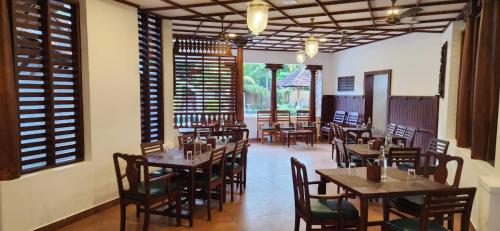 a restaurant with wooden tables and chairs and windows at Kumarakom Tharavadu - A Heritage Hotel, Kumarakom By Perfect Stays in Kumarakom