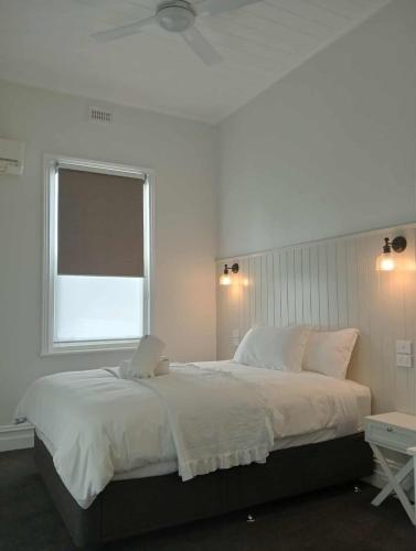 a white bedroom with a large bed with a window at Honeysuckle Inn - Violet Town in Violet Town
