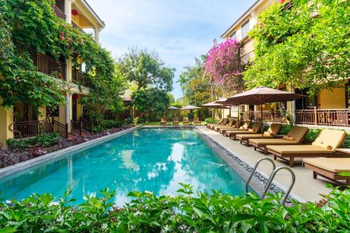 a pool with chairs and umbrellas next to a building at Ahoy Hoi An Boutique Resort & Spa in Hoi An