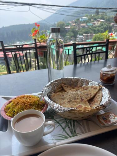 a table with a plate of food and a cup of coffee at Sharda House in Manāli