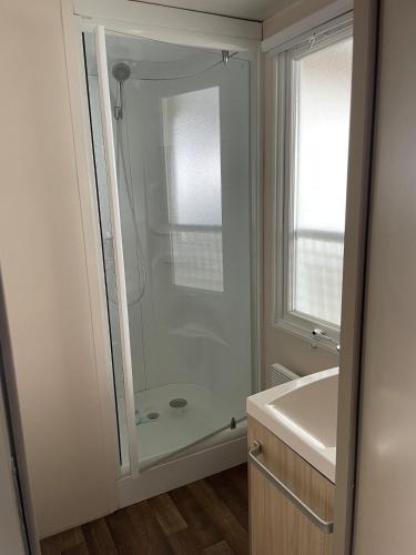La salle de bains est pourvue d'une douche et d'un lavabo blanc. dans l'établissement Mobil home dans camping 4 étoiles au calme, à Saint-Hilaire-de-Riez