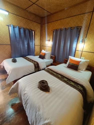 a room with three beds with white sheets and a bag on them at MG Guesthouse in Sukhothai