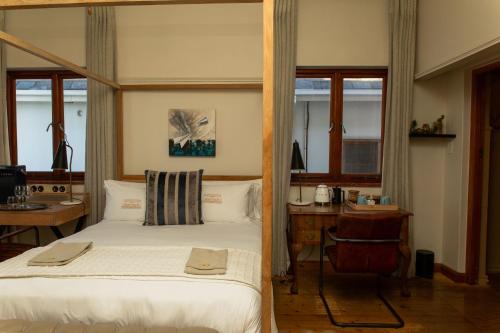 a bedroom with a bed and a desk and windows at Sonnekus Boutique Hotel & Bistro in Kalk Bay